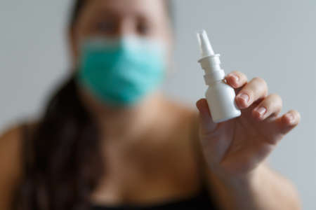Girl in a mask on a white background holding a nasal drops, medical themeの写真素材