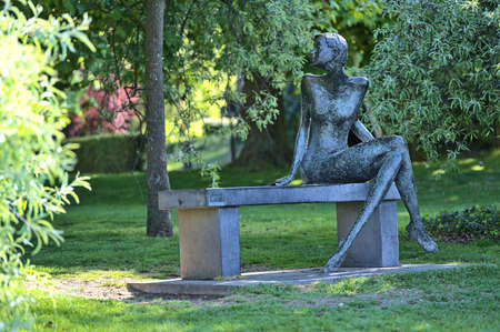 Dublin, Ireland - April 30, 2021: Beautiful front view of the Rendezvous sculpture at University College Dublin in various green spring colors beside UCD lake. Sculpture of woman sitting on benchのeditorial素材