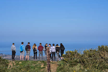 Co. Dublin, Ireland - April 2, 2021: Beautiful bright view of group of teenagers in a row seeing scenic views on Shankill and Irish Sea from Ballycorus Lead Mines on sunny day. High resolutionのeditorial素材