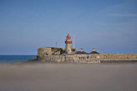 Beautiful creative evening view of red East Pier lighthouse in Dun Laoghaire harbor seen from West Pier, Dublin, Ireland. Copy space. Soft and selective focusの写真素材