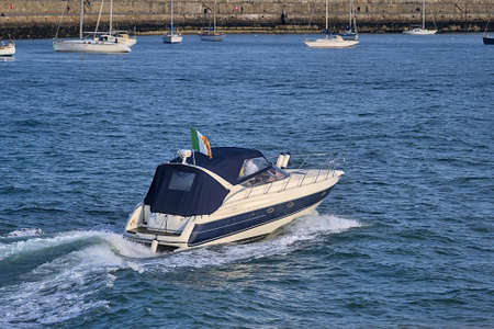 Beautiful evening view of single moving boat yacht on the water with Irish flag in Dun Laoghaire harbor, Dublin, Ireland. Soft and selected focusの写真素材