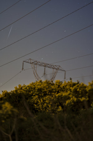 Beautiful night view of power lines, electric transmission pylon, falling Lyrid meteor and spring yellow flowering gorse (Ulex) in Ticknock, County Dublin, Ireland. Soft and selective focusの写真素材