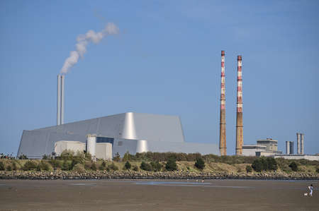 Beautiful closeup bright view of iconic Poolbeg CCGT station chimneys and Covanta Plant (Dublin Waste to Energy) against clear blue sky seen from Sandymount Beach, Dublin, Ireland. Walking peopleの写真素材