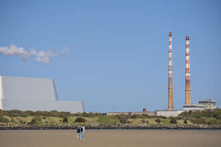 Beautiful closeup bright view of iconic Poolbeg CCGT station chimneys and Covanta Plant (Dublin Waste to Energy) against clear blue sky seen from Sandymount Beach, Dublin, Ireland. Walking peopleの写真素材