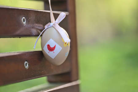 Beautiful closeup view of light beige plastic decorative Easter egg tied with ribbon on dark brown bench at university campus, Belfield, Dublin Ireland Soft and selective focusの写真素材