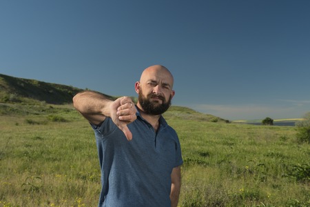 Caucasian white man with beard and mustache showing thumb down. blue skyの写真素材
