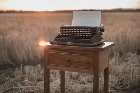 typewriter on a walnut bedside table in a wheat field at sunsetの写真素材