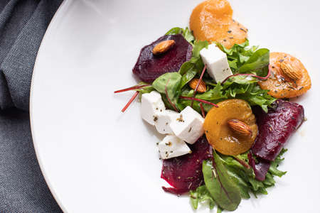salad with herbs, cheese, nuts, dried apricots, nuts, beets, on a white plate, gray backgroundの写真素材