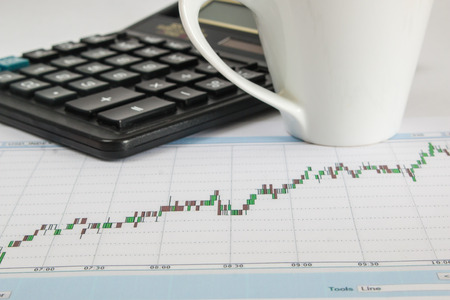 Business graph on a white background with calculator and cup of coffeeの写真素材