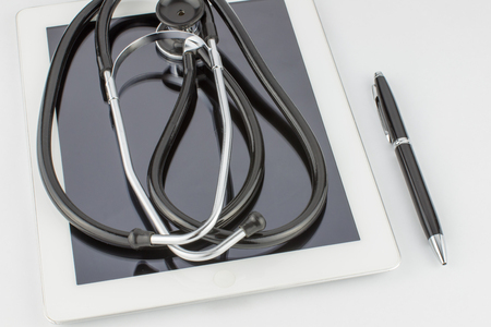 Stethoscope is reflected in the glass tablet computer, next is the pen on white background close upの写真素材