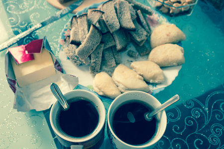 Cups of coffee, homemade curd cakes, crackers and butter with a knife on a glass table.