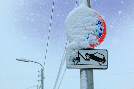 Road sign a stop is forbidden and the tow truck is carried by snow on a sky background.の写真素材