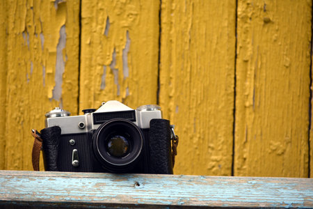 Vintage old camera weighs on a strap on the background of an old yellow wooden wall.