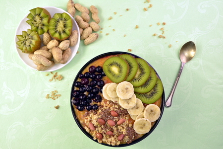Breakfast with muesli, acai blueberry smoothie and kiwi, banana, fruits on green background. Healthy food concept.の写真素材