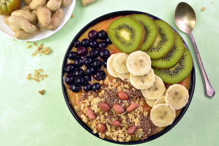 Breakfast with muesli, acai blueberry smoothie and kiwi, banana, fruits on green background. Healthy food concept.の写真素材