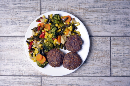 Meat patties with vegetables on a white plate on a gray background.の写真素材