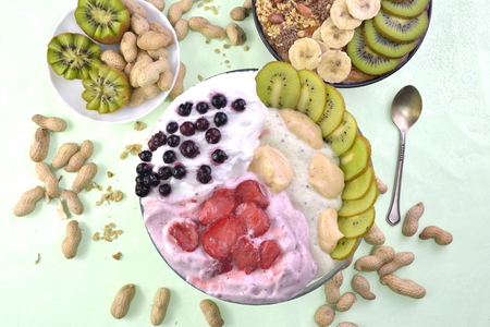 Breakfast with muesli, acai blueberry smoothie and kiwi, fruits on green background. Healthy food concept. Flat lay, top vie.の写真素材