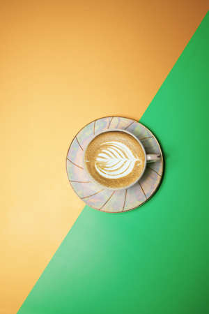 cup with coffee and cream in the form of a petal on a green-yellow backgroundの写真素材