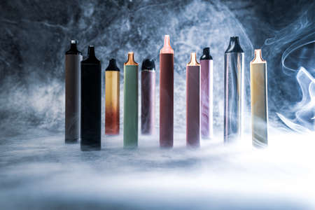 multicolored electronic cigarettes vape on dark background with smokeの写真素材