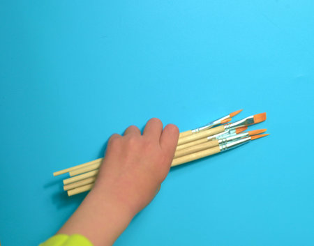 child holding brushes for painting on a blue backgroundの写真素材