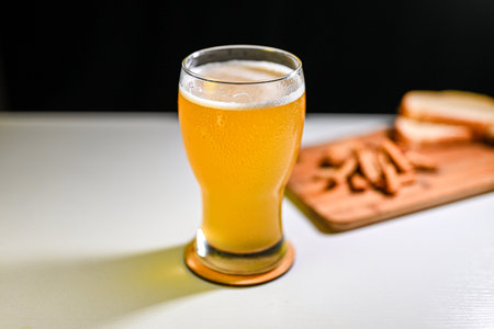 glass of beer on a light table in a pub with a snack on a dark backgroundの写真素材