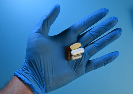 hand in blue medical glove holding several pills