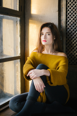 beautiful girl in a yellow sweater sitting near the windowの写真素材