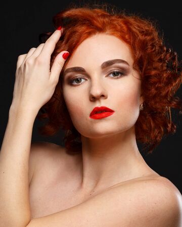 Closeup portrait of a beautiful red-haired girl half-turned over black background.