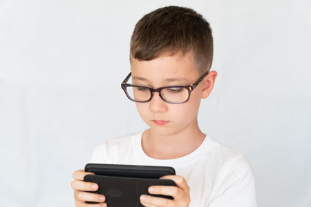 School boy looks handsome smartphone video, in glasses, dressed in white shirt, on white background,...