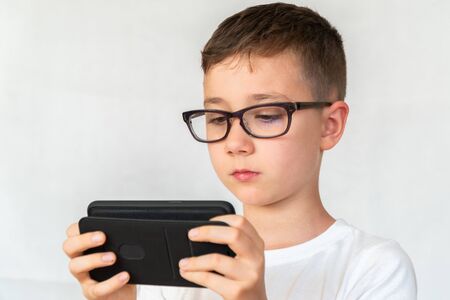 School boy looks handsome smartphone video, in glasses, dressed in white shirt, on white background, screams in frightの写真素材