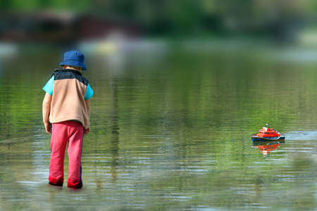 Boy gets in water to get his RC model.の写真素材