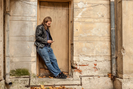 Blond long hair and beard young adult hipster man listening music. Outdoor, urban scene.の写真素材