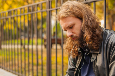 Blond long hair and beard young adult hipster man listening music. Outdoor, urban scene.の写真素材