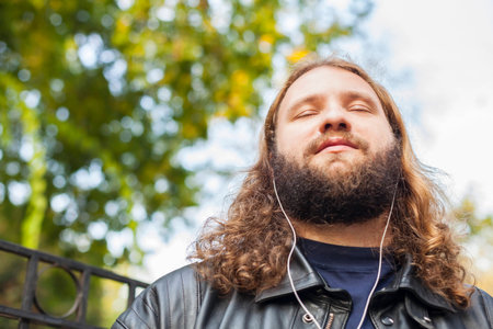 Blond long hair and beard young adult hipster man listening music. Outdoor, urban scene.