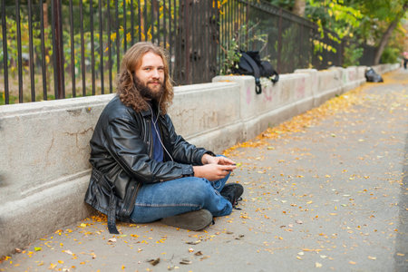 Blond long hair and beard young adult hipster man listening music. Outdoor, urban scene.の写真素材