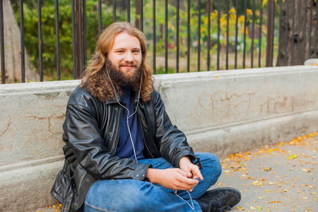 Blond long hair and beard young adult hipster man listening music. Outdoor, urban scene.の写真素材