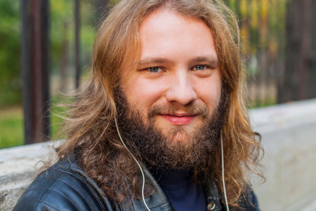 Blond long hair and beard young adult hipster man listening music. Outdoor, urban scene.の写真素材