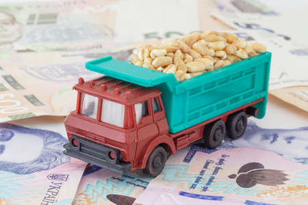 toy truck loaded with wheat grains standing on heap of Ukrainian banknotesの写真素材