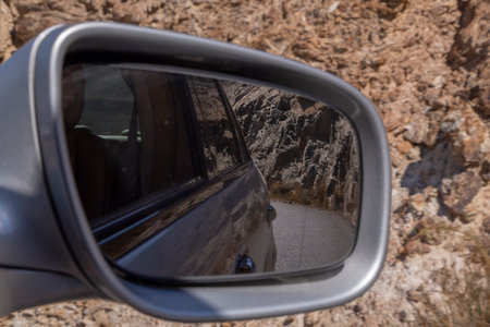view on road and rocks in wind mirror of car going by dangerous roadの写真素材