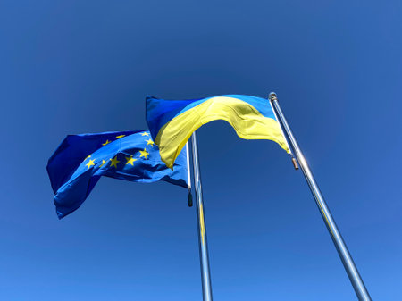 Ukrainian and European Union flags waved on flagpoles against blue skyの写真素材