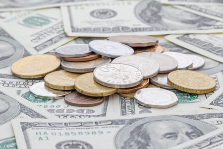 heap of different countries coins lying on one hundred US dollars banknotesの写真素材