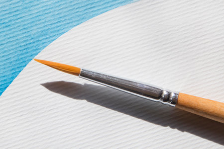 closeup of round paint brush laying on white paper with blue strokeの写真素材