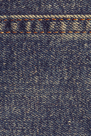 abstract vintage backdrop: close up of blue aged jeans texture with seam at topの写真素材