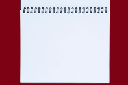 close up of  blank white page of opened sketchbook with spiral binder against red background