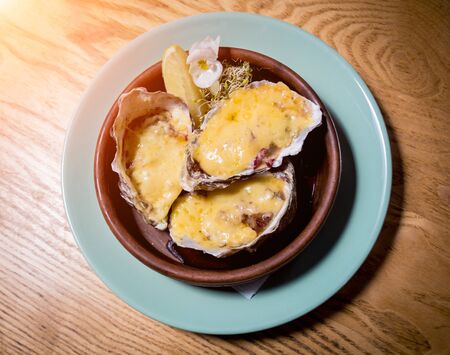 Fresh oysters under cheese on a plate with ice and flowers. Restaurantの写真素材