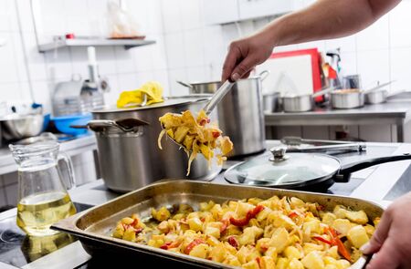 Chef cooks fried potatoes with pieces of meat in a restaurant kitchenの写真素材