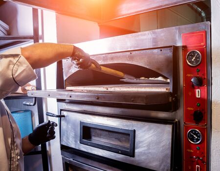 The process of making pizza. Chef baker puts raw pizza in the oven. Kitchen. A restaurantの写真素材