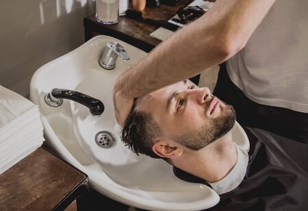 Young man with trendy haircut at barber shop. Barber washes customer head. Concept barbershop.の写真素材