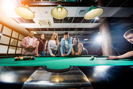 Group of young cheerful friends playing billiards.