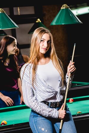 Young woman playing in billiard. Posing near the table with a cue in her handsの写真素材